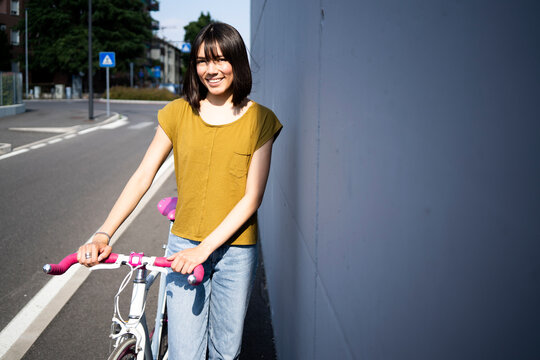 Young woman with bicycle standing near wall