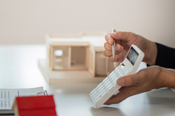 Real Estate Transaction. A professional reviewing plans with a calculator and model house.