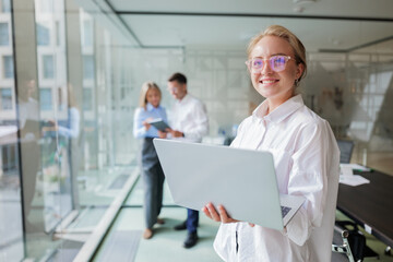 Smiling professional in modern office collaborates with colleagues while using laptop