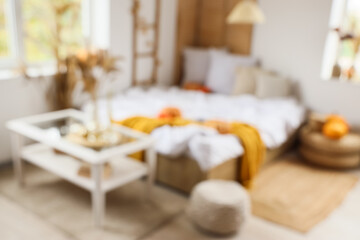 Interior of stylish bedroom with cozy bed, coffee table, ottoman and pumpkins, blurred view