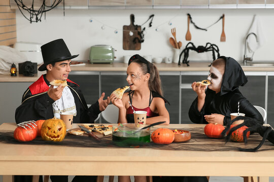 Kids dressed for Halloween eating pizza at party in kitchen