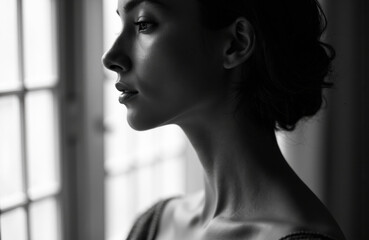 Fototapeta premium Woman in profile looking out window with natural light illuminating her face and neck