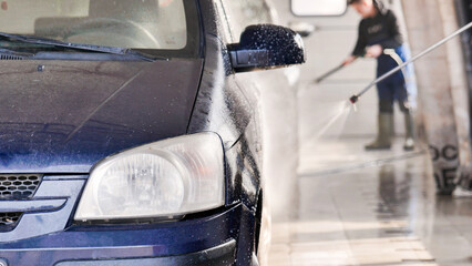 Car wash worker cleaning vehicle with high pressure water jet