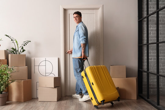 Young man with suitcase opening door in hall on moving day