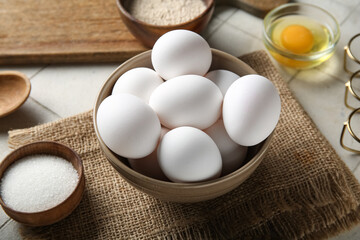 Bowl with raw chicken eggs and sugar on white tile background