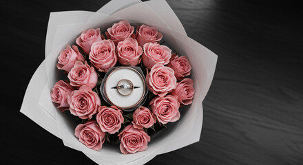 Wedding rings in pink rose bouquet on wooden table top view