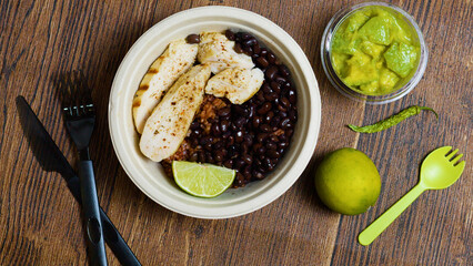 Disposable bowl featuring grilled chicken breast, black beans, brown rice, and lime wedge, paired...