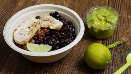 Seasoned chicken breast served on black beans and rice with lime, accompanied by guacamole, lime and chili pepper on a wooden table promotes a healthy and sustainable lifestyle