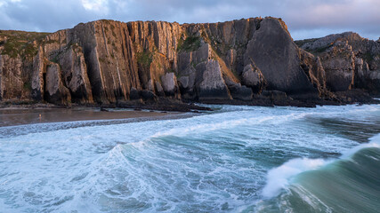 Ocean waves crashing on Praia da Adraga beach at sunset with cliffs in the background, located in...