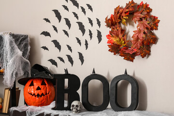 Different Halloween decorations and word BOO on fireplace near white wall in room