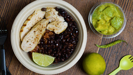 Colorful chicken bowl featuring brown rice, black beans, guacamole, lime wedge, chili pepper...