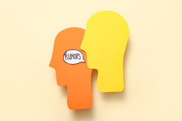Paper human heads and speech bubble with word RUMORS on beige background. Gossip concept