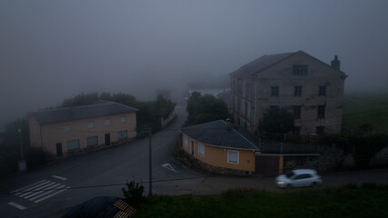 Driving through foggy evening streets in Tapia de Casariego, Spain, a white car creates a spooky,...