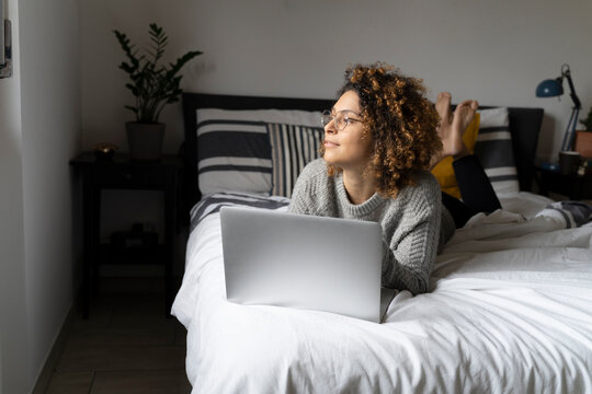 Woman lying on bed, using laptop, surfing the net