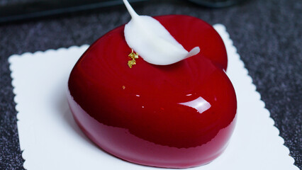Red, heart shaped mousse cake adorned with a white chocolate petal and gold flakes, resting on a...