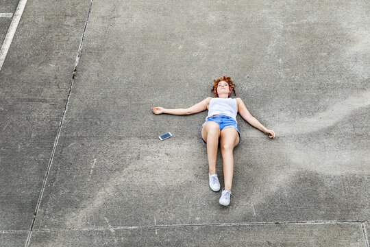 Young woman lying on parking level next to cell phone