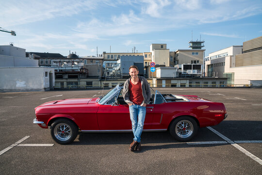 Portrait of smiling mature man leaning against his parked sports car