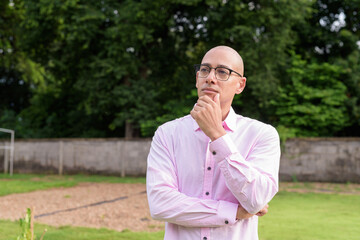Bald Hispanic man thinking and looking up with hand on chin outdoors