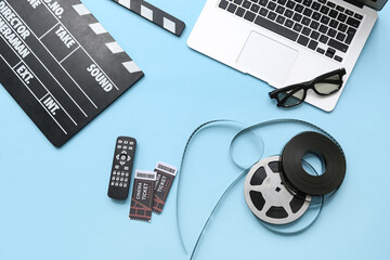 Movie clapper with cinema tickets, remote control, laptop and film reels on blue background