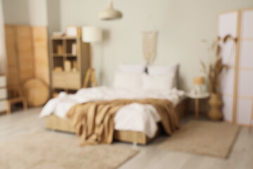 Interior of modern bedroom with bed, shelving unit and folding screens, blurred view