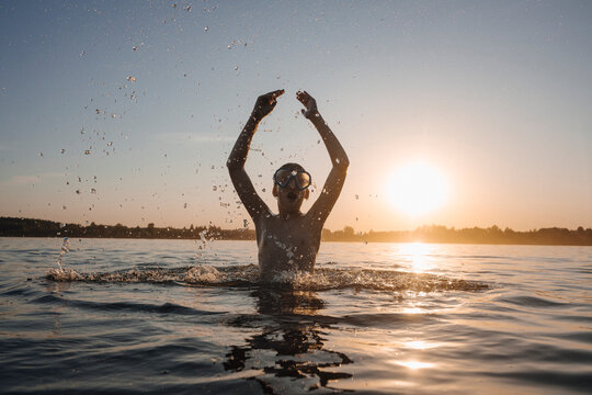 Teenage boy swimming and splashing in a lake at sunset enjoying summer