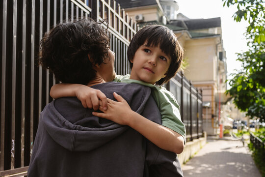 Mother holding and hugging son while walking outdoors in summer
