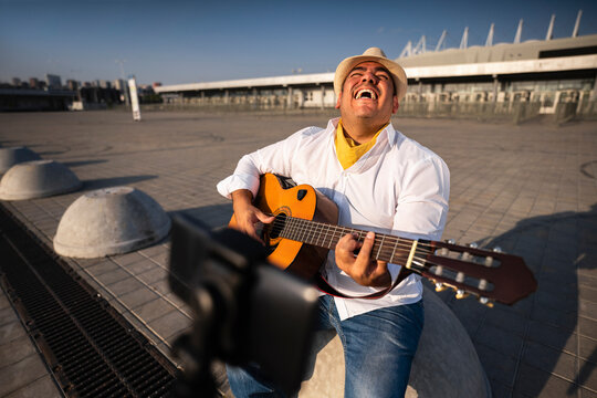 Cheerful guitarist holding guitar in front of mobile phone on tripod