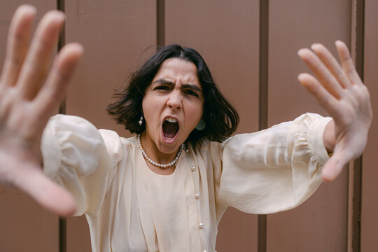 Woman showing stop gesture and screaming in front of wall