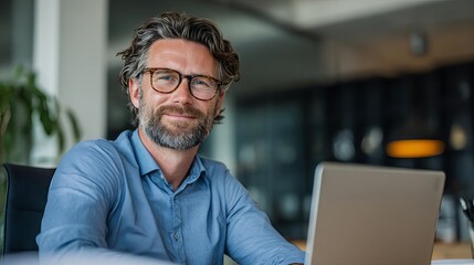 Obraz premium Confident businessman with glasses smiling at laptop in modern office, professional and successful