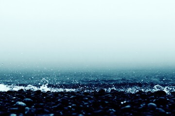 Misty ocean waves crash on a dark pebbled shore