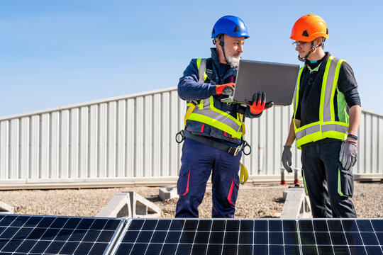 Technician with laptop discussing with colleague at solar power station
