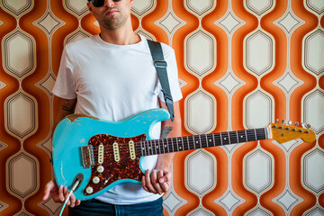 Young male musician holding guitar in front of wall