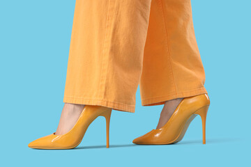Legs of young woman in yellow high heels on blue background