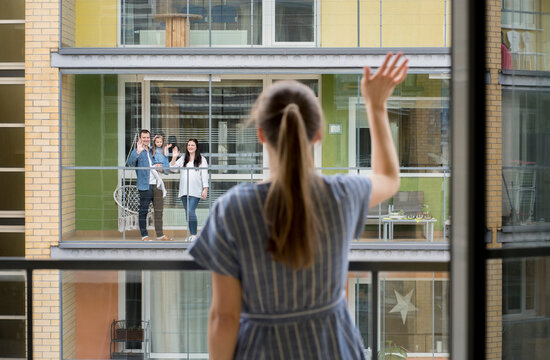 Back view of woman standing on balcony waving to her neighbours