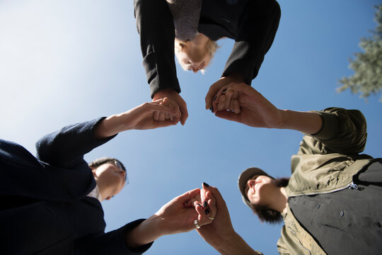 Worm's eye view of three women holding hands under blue sky