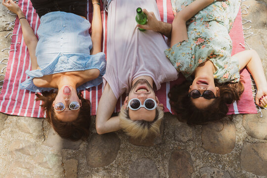 Smiling man lying amidst female friends sticking out tongue while relaxing on blanket