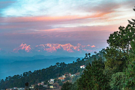 Panoramic view of a Himalayan town in a cold evening with snowcapped Nanda Devi Mountain range in the backdrop with colorful evening sky