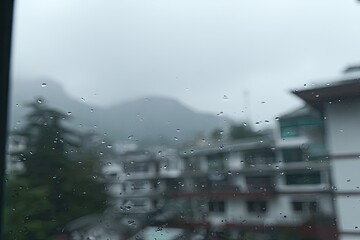Rain-streaked window view of misty mountains and buildings