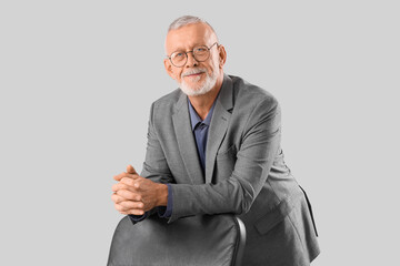 Senior businessman with clasped hands leaning on chair against grey background