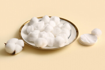 Plate with cotton balls, pads and flower on beige background