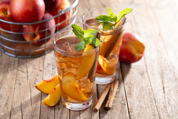 Refreshing peach iced tea in glass with ice cubes and cinnamon on wooden table