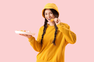 Young girl eating tasty nachos on pink background