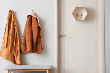 Interior of stylish hall with jackets, door, grey bench and key holder on door
