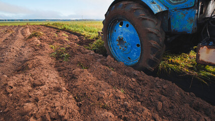 Blue tractor plowing fertile soil in field creating furrows for crops