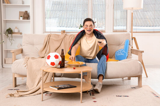 Male sports fan with German flag and potato chips watching football game on TV at home