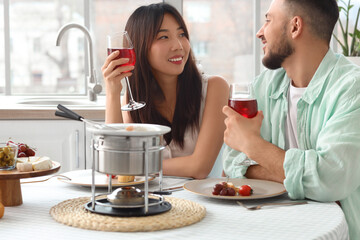 Young couple with snacks and cheese fondue drinking wine at home