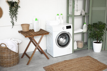 Stylish laundry room with modern washing machine, houseplant and bottles of detergent