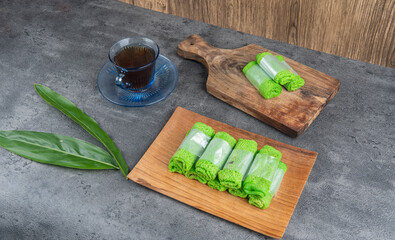 Delicious Indonesian dadar gulung dessert neatly served on a wooden plate with coffee and leaf...