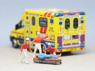 Mini toy of action figure at table with blurred background. Miniature photography concept design. Minifigure of paramedic crew character with ambulance. Rescuing patient.