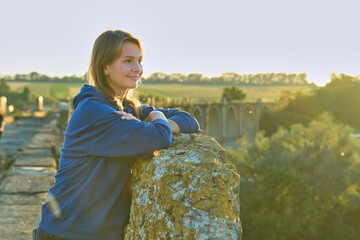 A girl stands near an old arched bridge